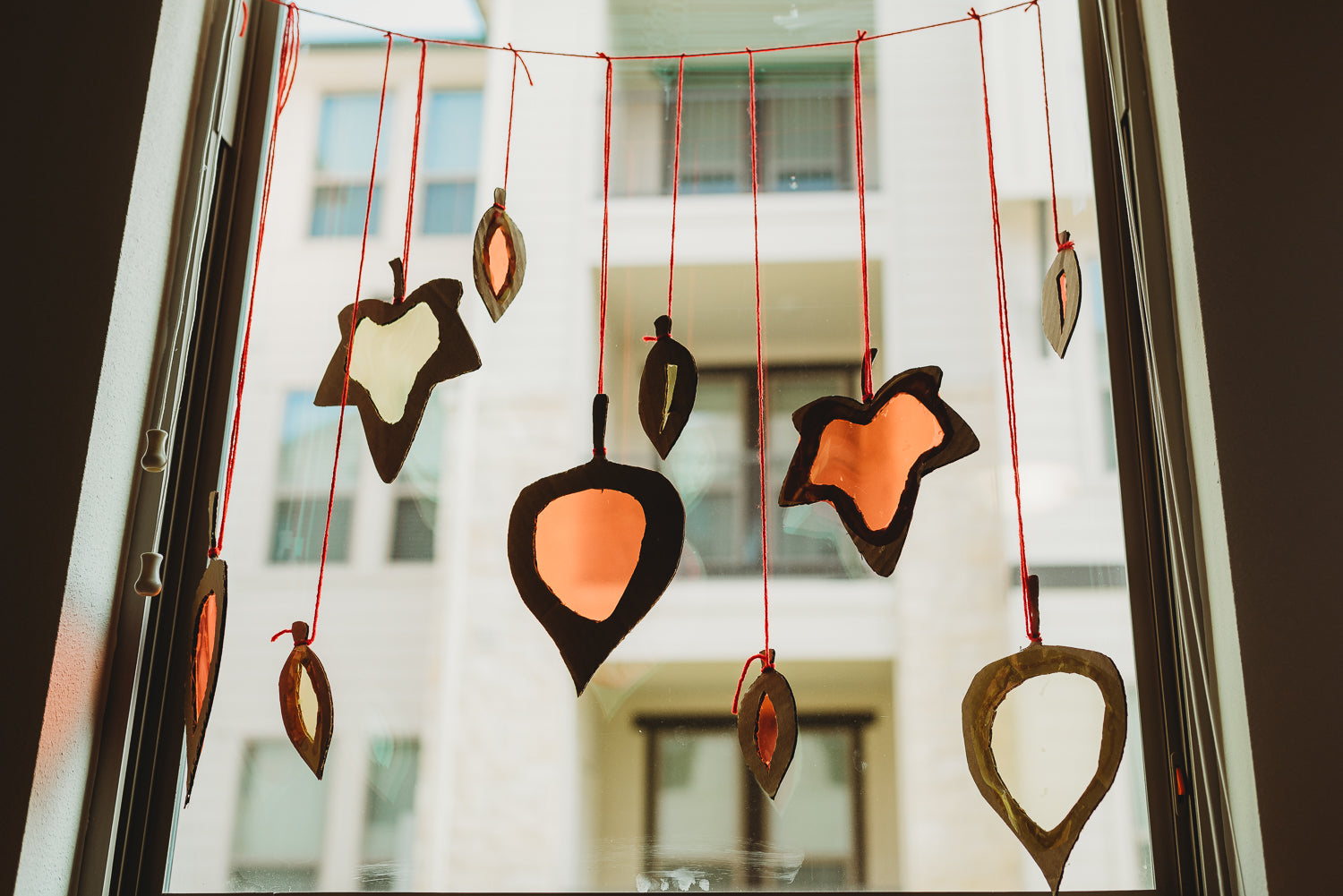 Series of cardboard leaves hanging from red yarn in a window.