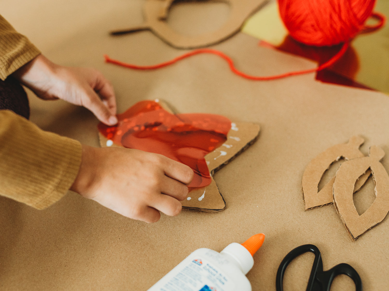 A child glues biodegradable red cellophane to cardboard for an eco-friendly fall craft project.