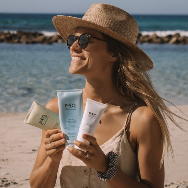 Smiling woman, walking on the beach, holding 3 tubes of People4Ocean sun cream in her hand