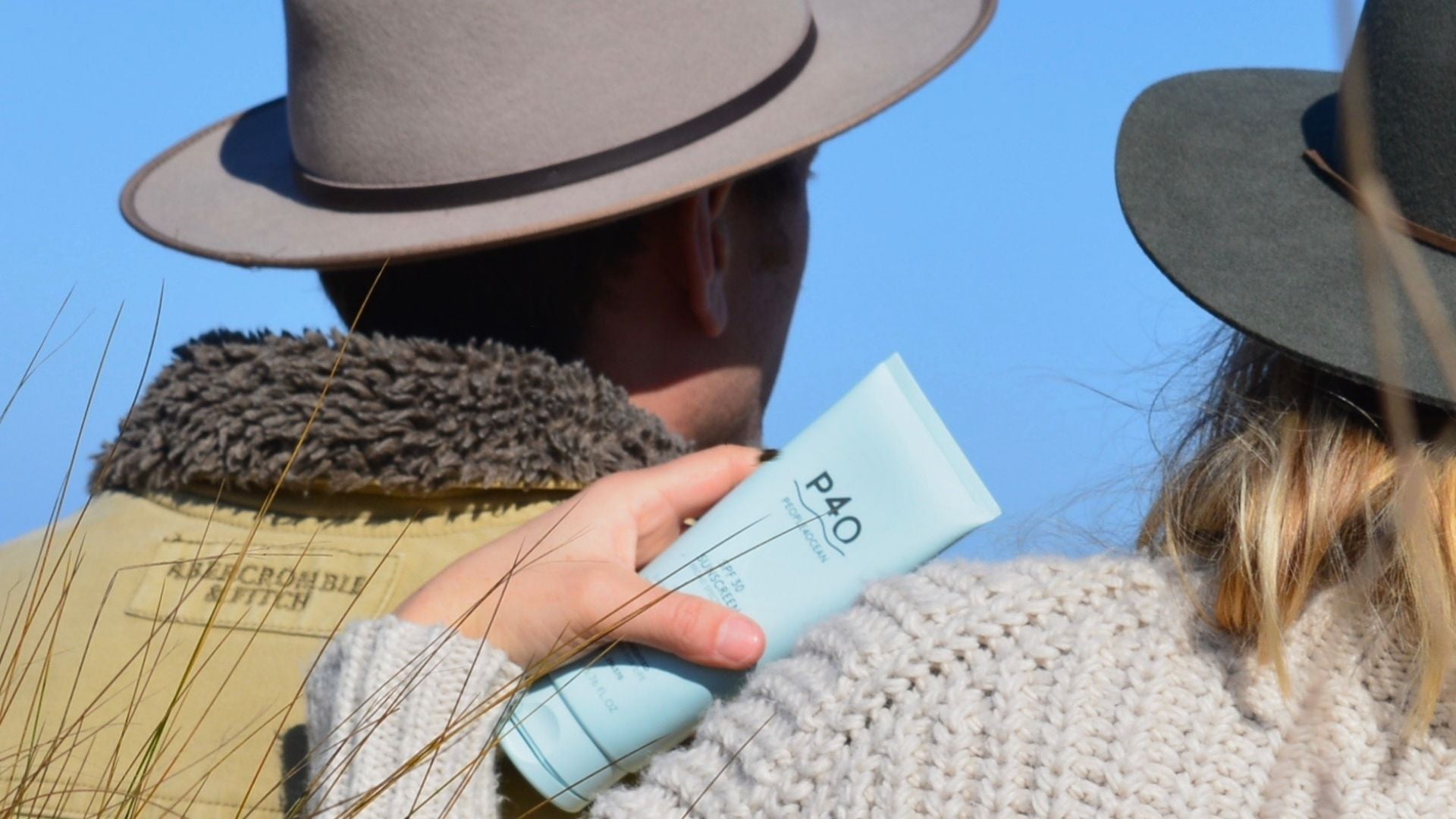 The back of two people holding sunscreen and wearing winter clothes