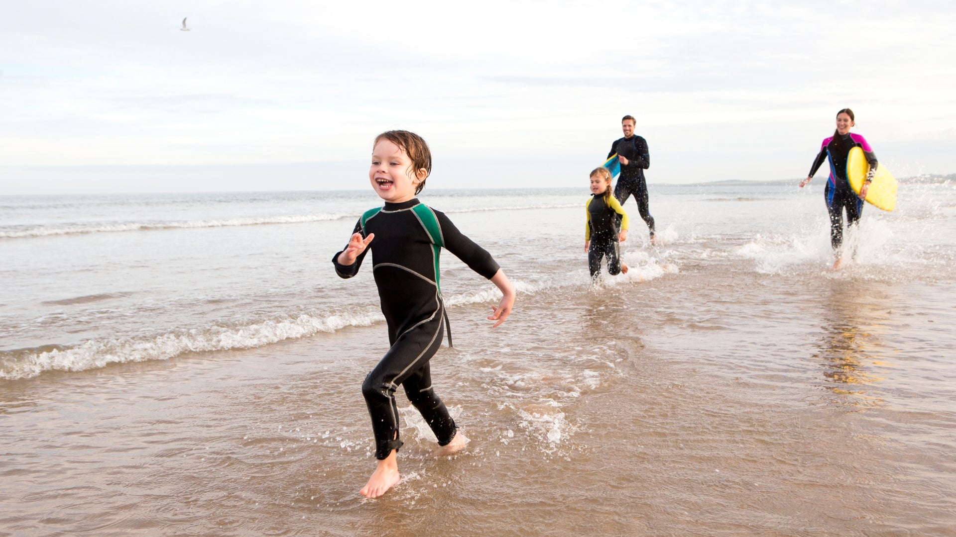 Kids in wetsuits running along the beach