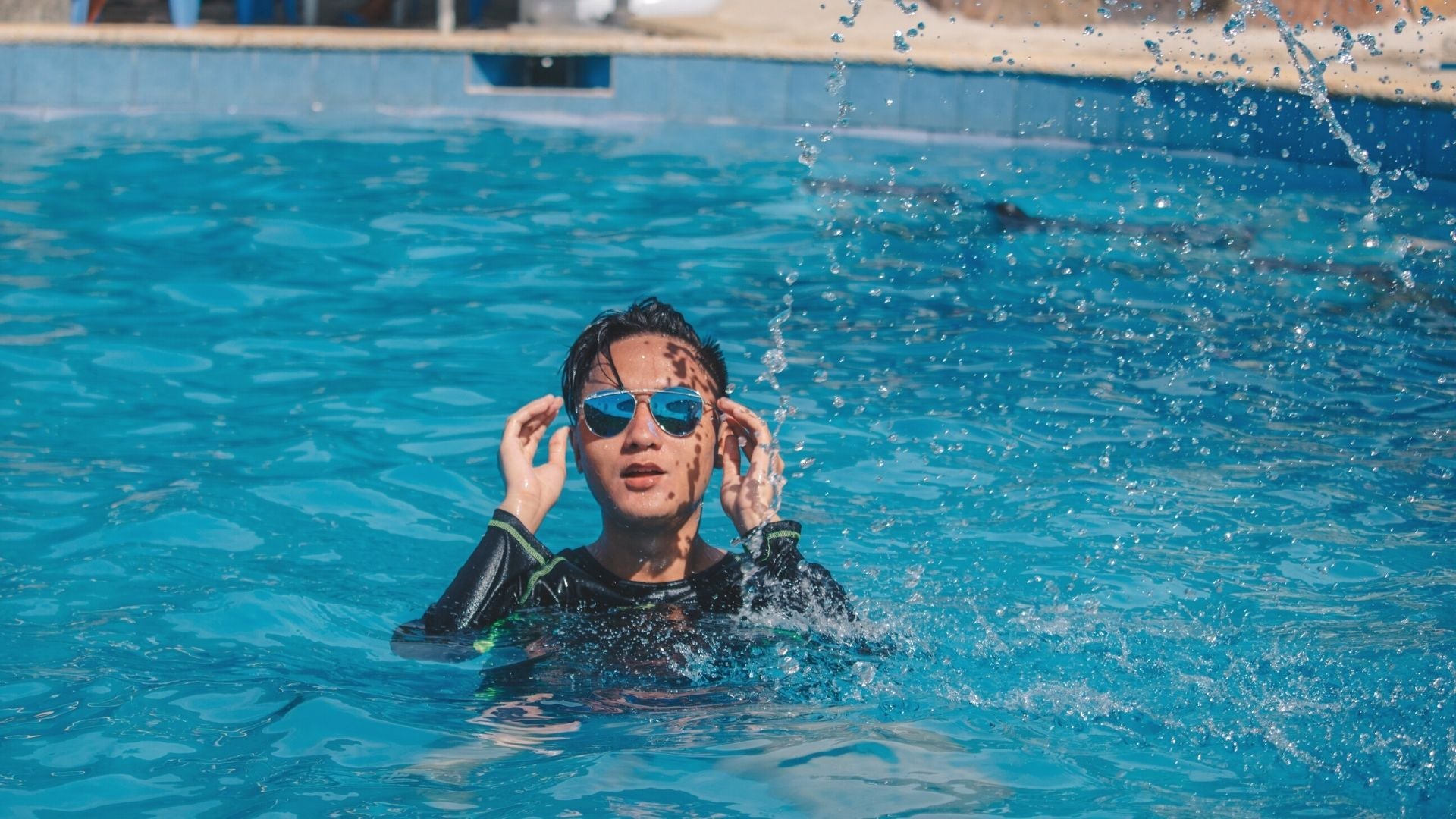 A woman in a pool with blue tinted aviator sunglasses on