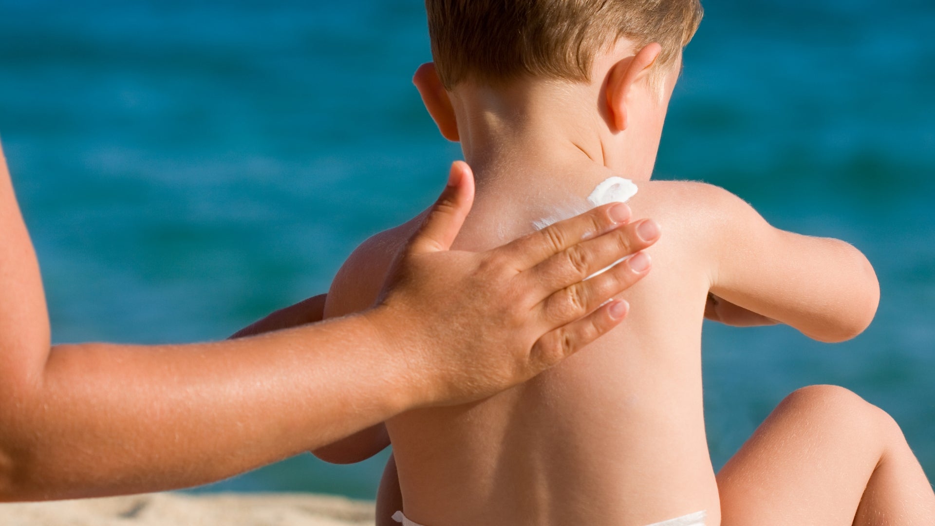 Woman's arm applying sunscreen to her young son's back