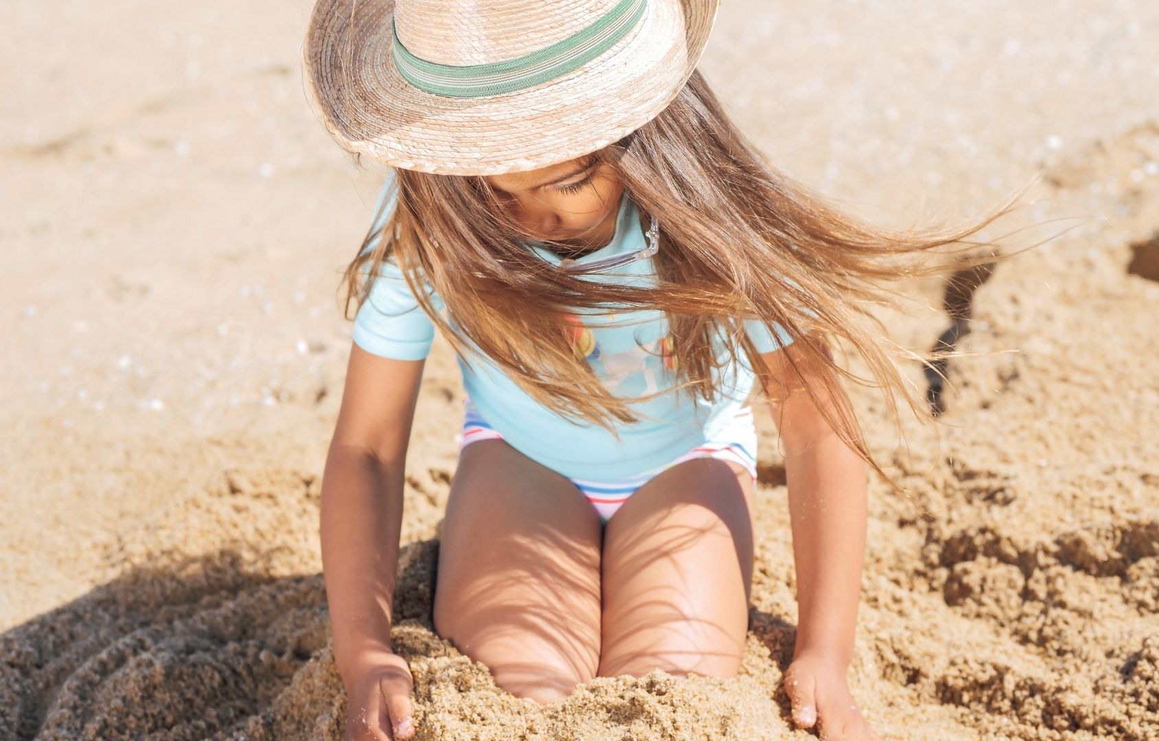 Girl sitting on the sand in sunscreen and a hat