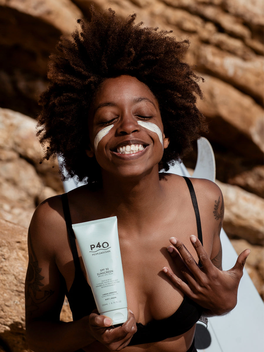 Afroamerican lady applies sunscreen on her face
