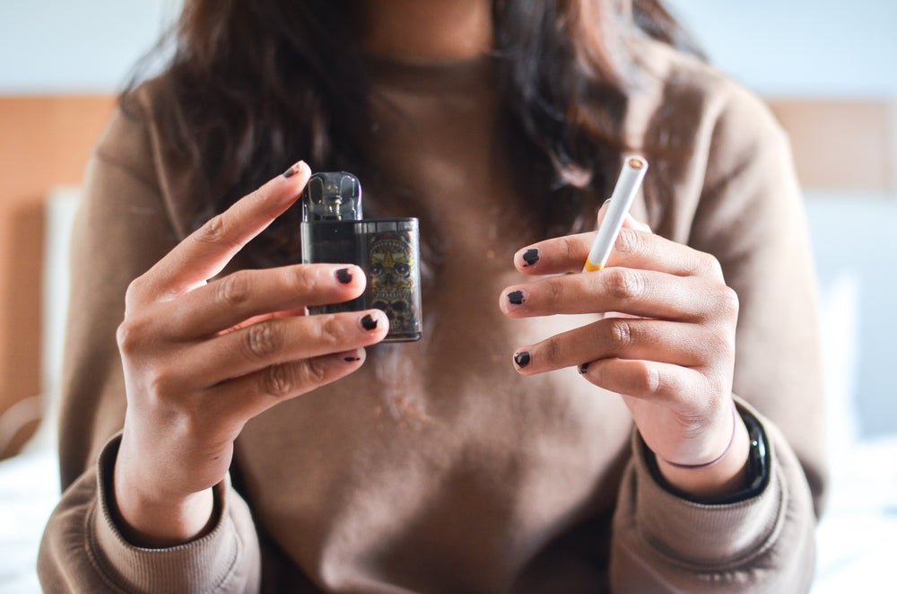 vaping vs a cigarette - woman holding both, one in each hand