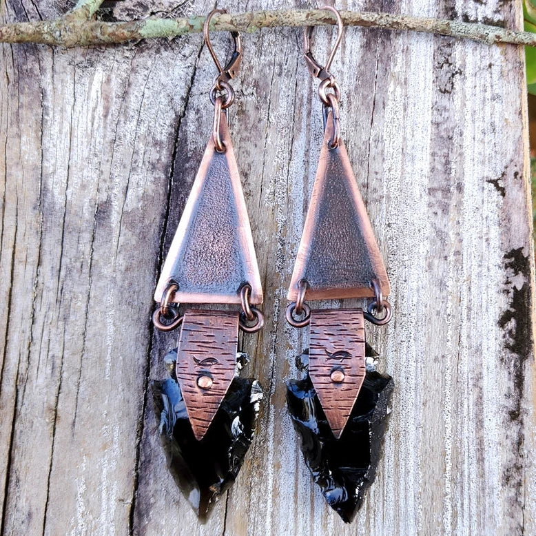 Onyx and copper arrowhead earrings on a wood background.