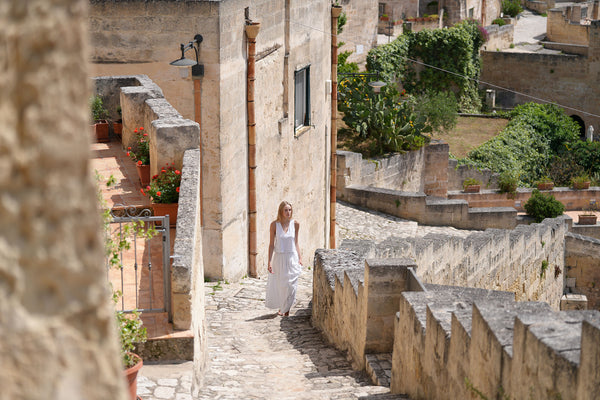 A woman in a white dress walks up ancient stone steps.