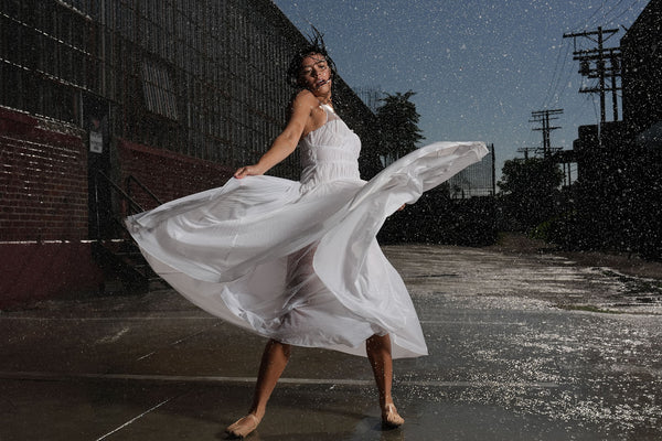 A woman in a white dress dances in the rain
