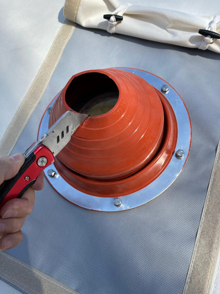 quelqu'un utilise un cutter pour couper un solin en silicone orange afin de l'adapter au tuyau de poêle