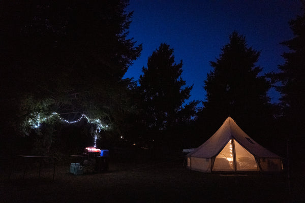 Une scène nocturne avec une tente familiale en toile éclairée sur fond d’arbres en silhouette.