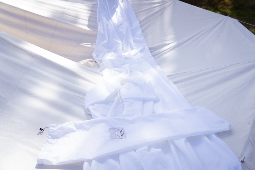 Une housse anti-mouches en nylon blanc est déroulée sur une tente cloche en toile dont le mât central a été temporairement retiré.