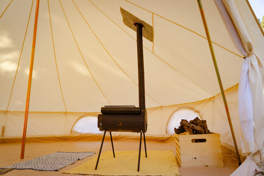 Un poêle à bois noir est installé à l’intérieur d’une tente cloche en toile.