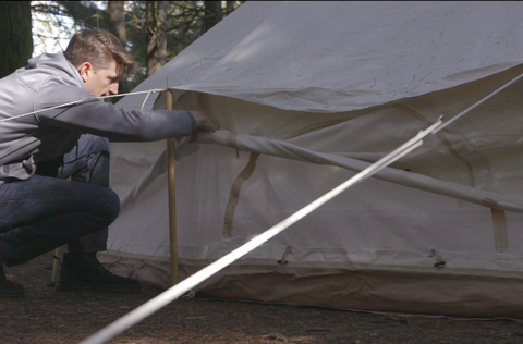 Une personne enroule les murs d’une tente cloche en toile.