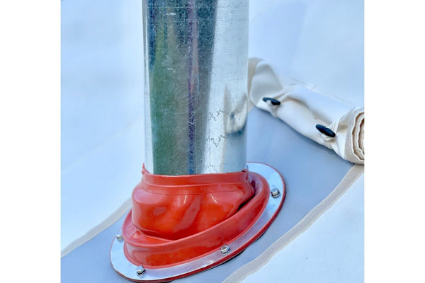 un solin en silicone rouge contre un solin en acier inoxydable argenté et un tuyau de poêle en métal traversent le haut d'une tente en toile