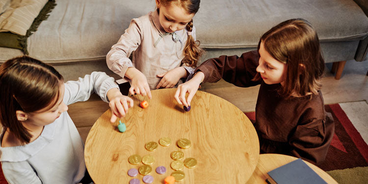 three young girls playing a board game while sitting around a small round table