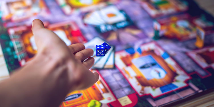 hand throwing a die on a board game; the background is blurred out
