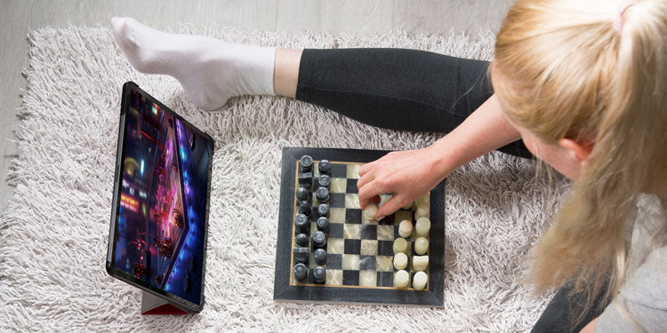 a top down photo of a girl playing physical chess and a  futuristicvirtual game on a tablet