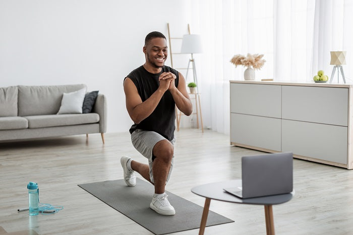 Mann trainiert auf Fitnessmatte mit Laptop