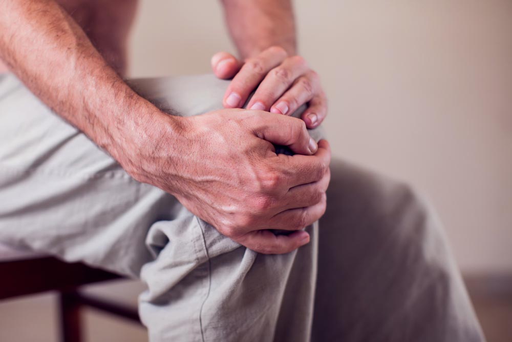 Man who suffers from arthritis grips aching knee.