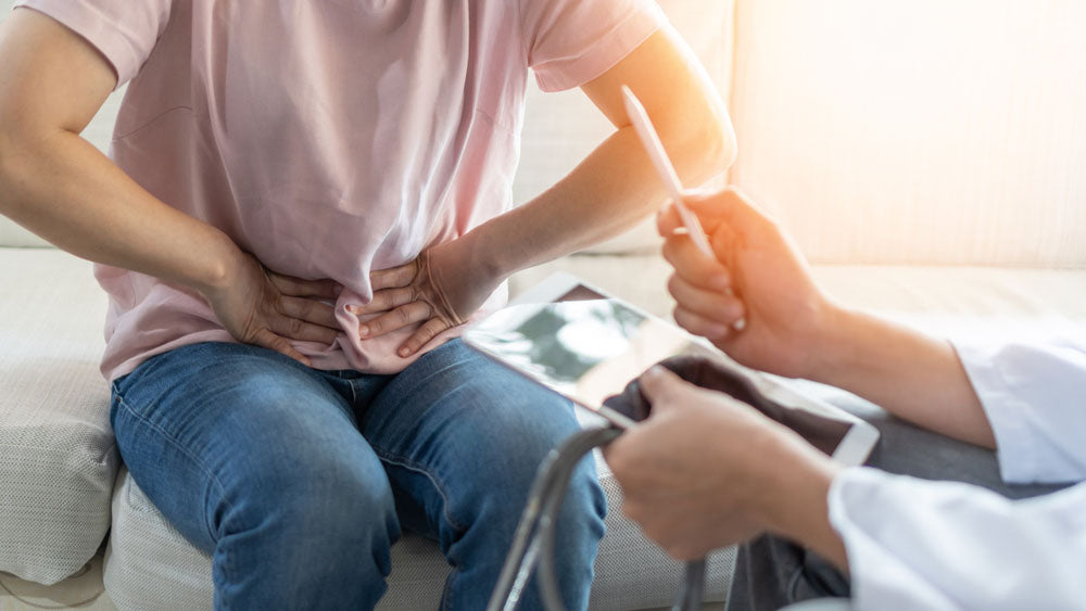 Patient sits with doctor and holds hands to stomach in sign of discomfort