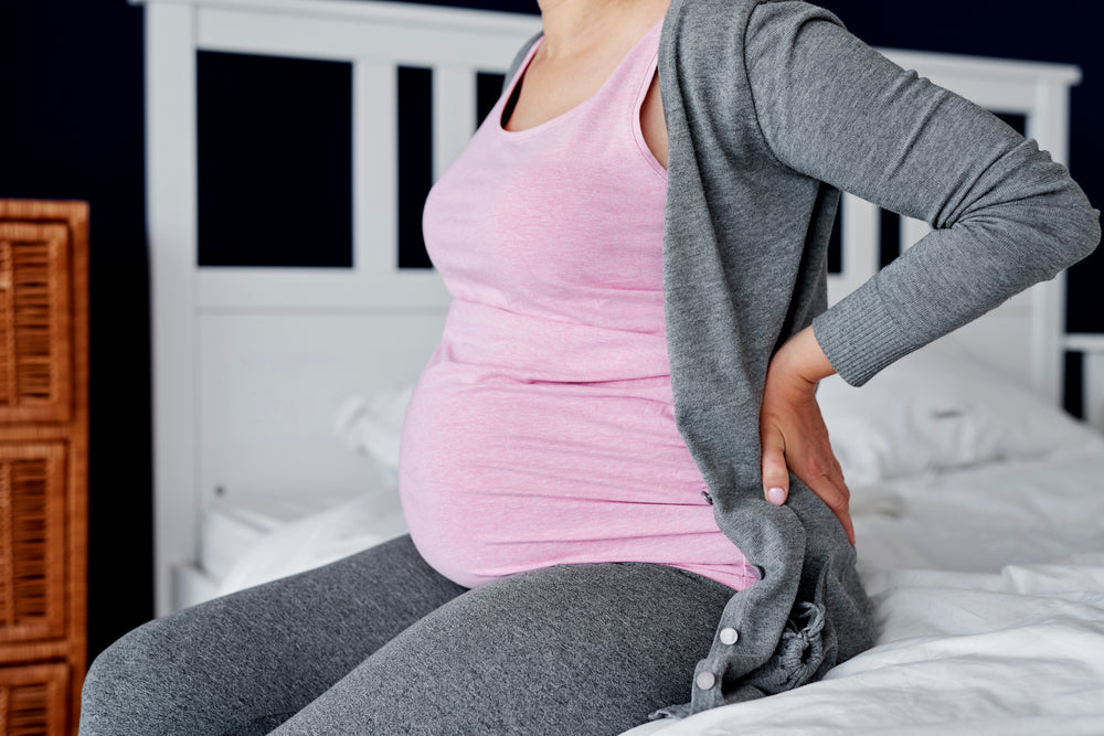 pregnant woman suffering from back pain sitting on a bed