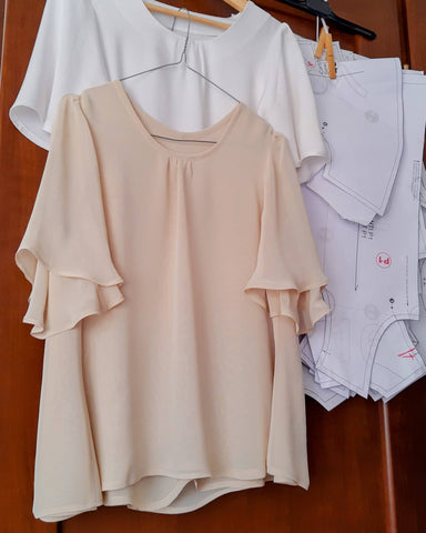 A chiffon blouse with a flared shape in shades of ochre is hanging on a hanger next to paper sewing pattern pieces. 