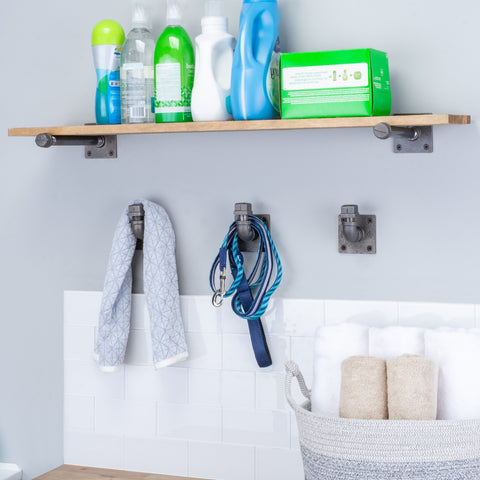 A well-organized laundry room with a wall-mounted shelf holding cleaning supplies and industrial pipe hooks for hanging towels and dog leashes.