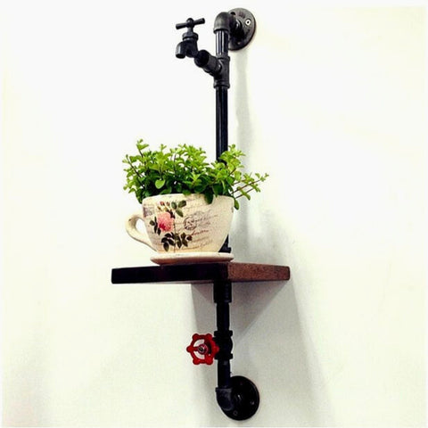 A small industrial-style pipe shelf with a faucet design supports a decorative plant in a teacup, adding a rustic and unique touch to wall decor.