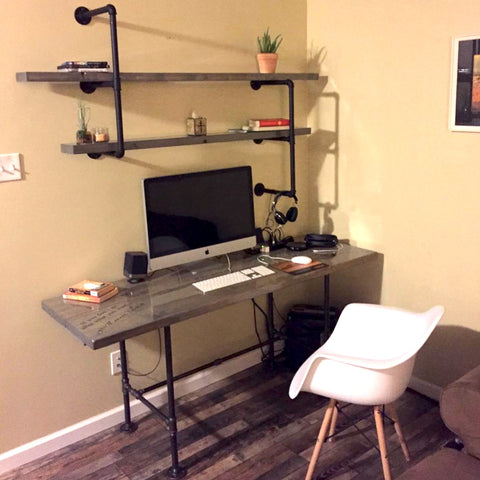 Image of a modern home office featuring a desk with industrial pipe legs, accompanied by matching floating shelves adorned with plants and books.