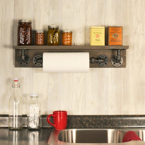 Image of a wooden floating shelf with industrial pipe brackets, displaying assorted mason jars, vintage tea and gelatin boxes, and a paper towel holder in a kitchen.