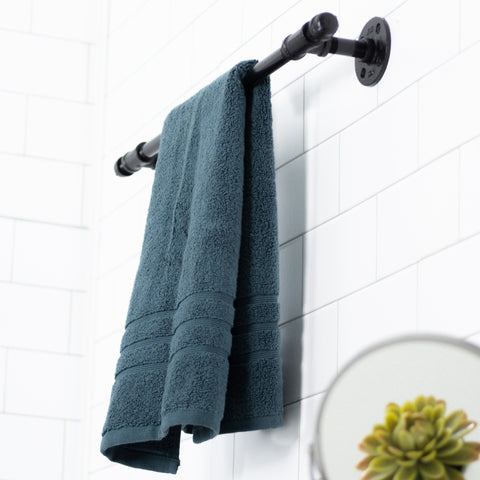 Image of a stylish towel rack crafted from industrial pipes, holding a plush blue towel against a clean white tiled bathroom wall.