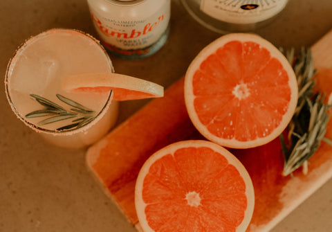 cocktail with cut grapefruit, can of sparkling water, and fresh rosemary