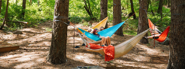 Four Roo Double hammocks, Sky blue, ember orange, yellow, and tan, hung between trees for a group campout with friends.