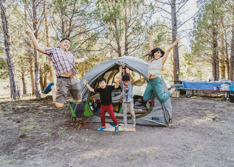 Dr. Wong and her family jumping in front of tent outside.