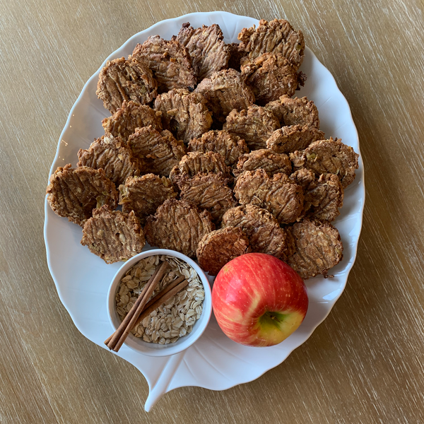 Homemade Dog Treats arranged on a white leaf plate with apple, cinnamon & oatmeal trimmings.