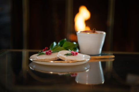 Speciality holiday cookies sitting next to ceramic mug in front of a fire