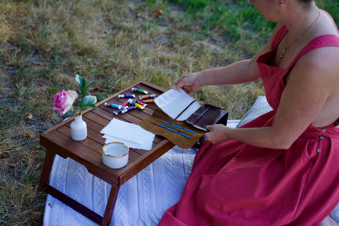 Artist kneeling on a picnic blanket picking up her painters palette
