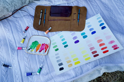 White porcelain watercolor palette with leather wrap sitting on top of a picnic blanket