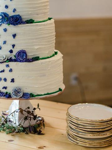 white three tier cake with blue flowers next to homemade pottery plates