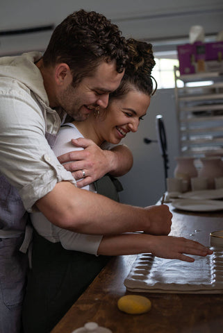 Man hugging woman from behind while packaging up holiday gift at Seattle small business