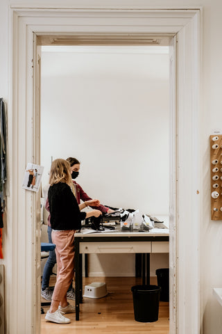 Foto zeigt zwei Mitarbeiterinnen von Lu-Couture, einer kleinen Näherei in Luzern. Sie stehen nebeneinander am Schneidetisch und diskutieren über das Material, das auf dem Tisch liegt.