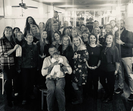 Group of people insidea restaurant posing for a photo with a man holding a baby at the front of the group.