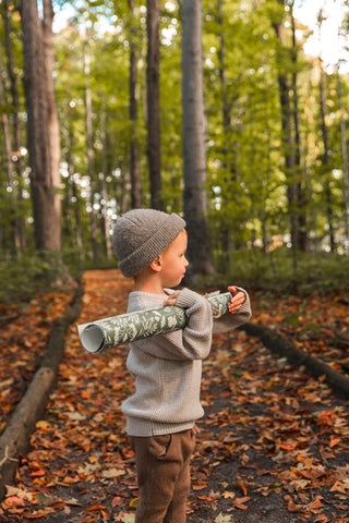 Little boy in the forest with a roll of wallpaper from the Woodland collection