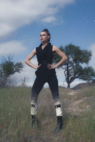 jaki stands in an open field with her hands on her hips, staring fiercly into the sky. she is wearing a pair of jeans with an ombre bleach wash and o-ring embelleshments at the knee. she is also wearing a handmade denim vest with an oversized collar, which perfectly compliments her mohawk hairstyle.