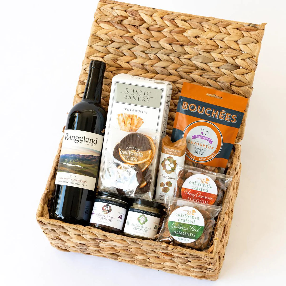 Basket with a bottle of wine, crackers, tapenade, bouches, almonds, dried oranges and a macadamia nut bar