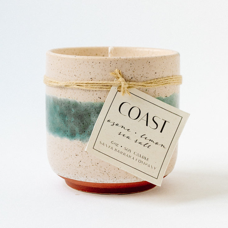 Candle in a ceramic cup with a blue stripe and tag tied around it.
