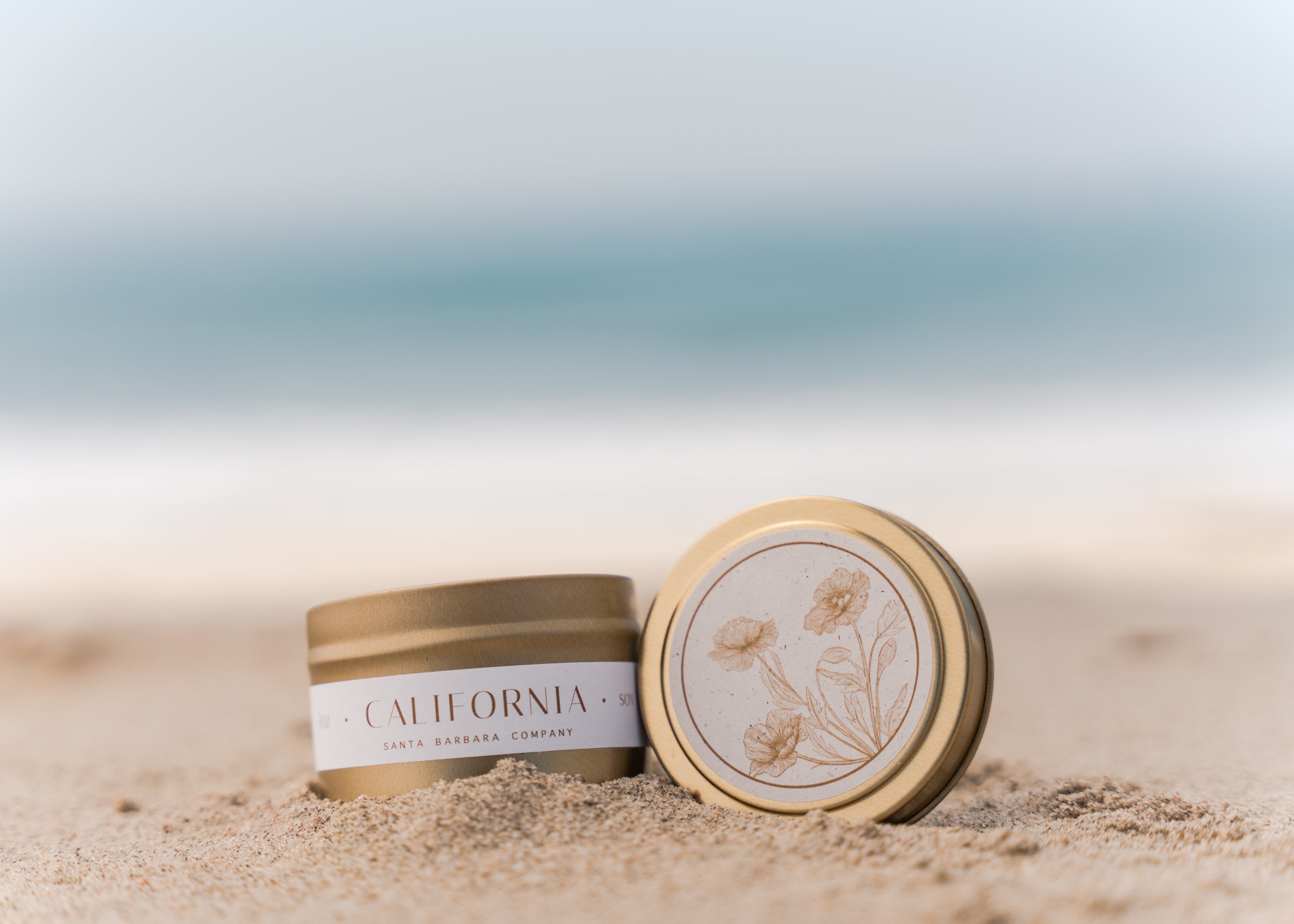 California candle in gold tin on sand oceanside