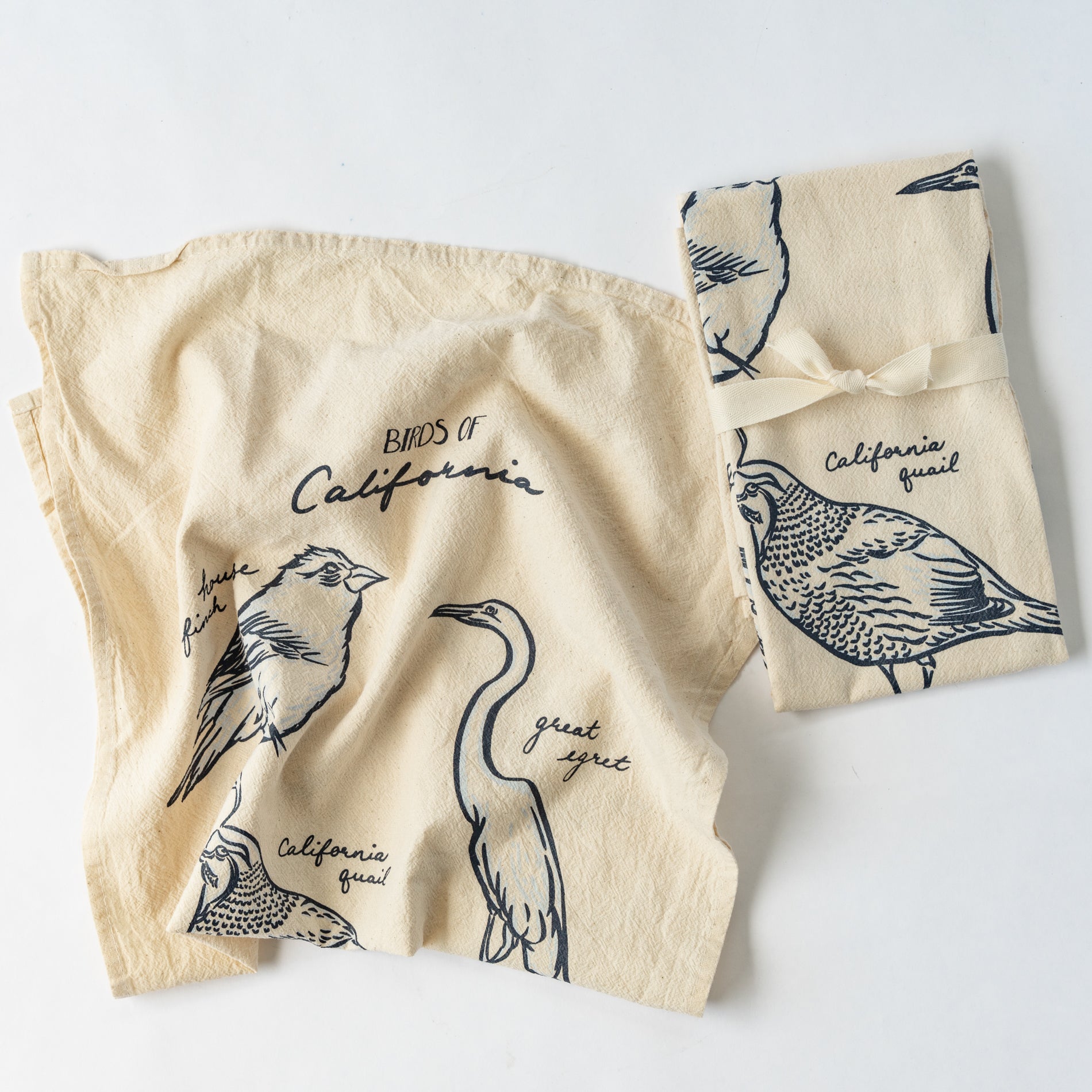 Two cream colored towels with bird illustrations against a white background