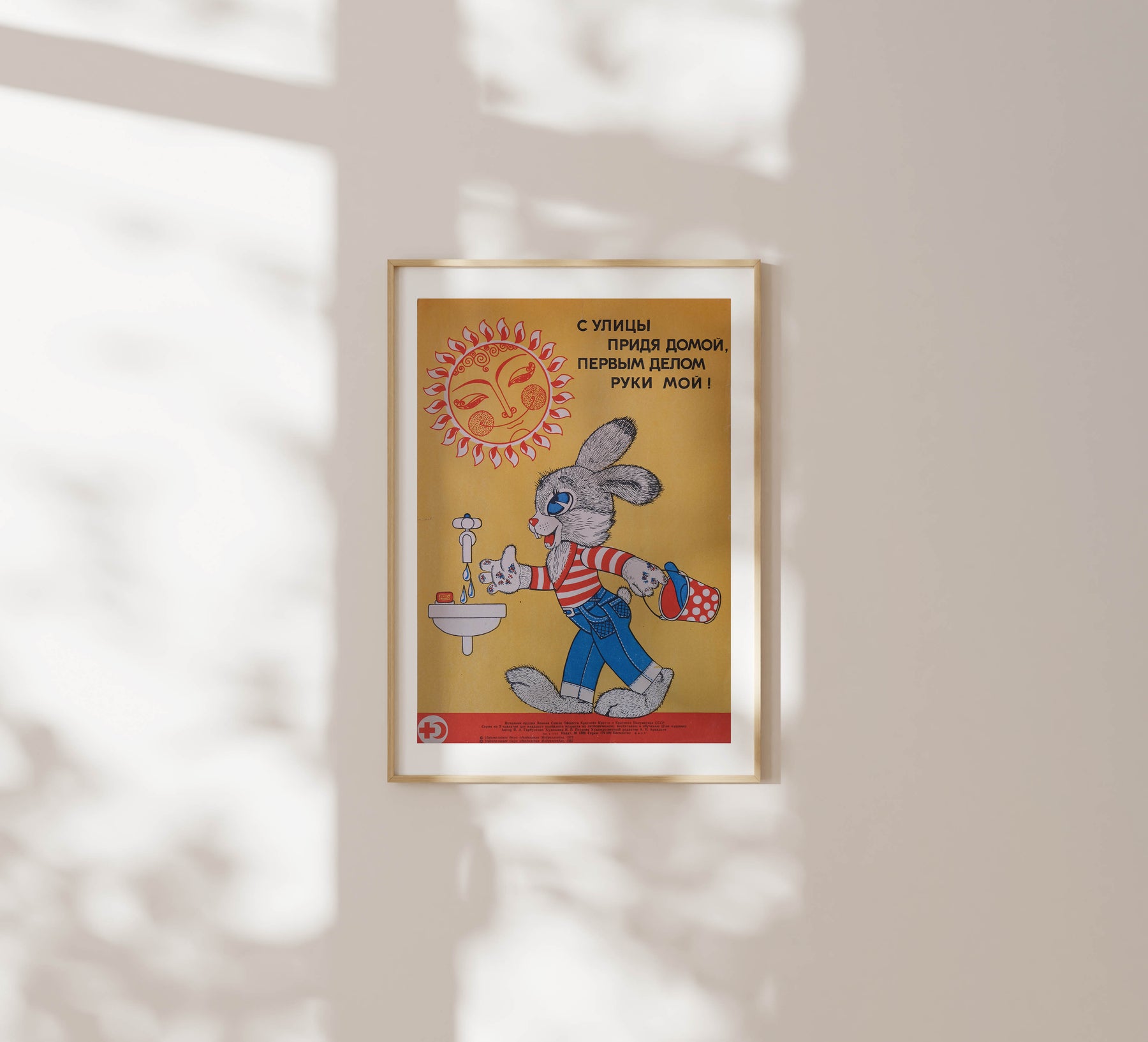 When Coming Home, the First Thing is to Wash Your Hands – Soviet Russia, hygiene awareness poster from 1982 by N, P, Petrova, featuring a basin and a rabbit against a yellow backdrop, framed in a wooden frame on a white wall with soft sunlight